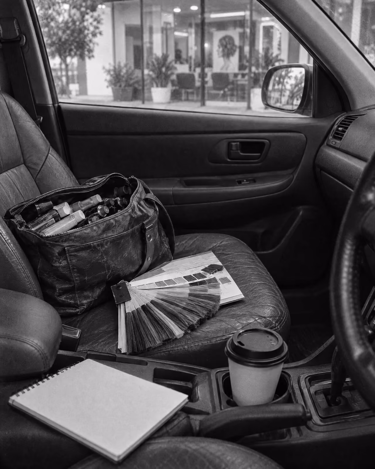 The passenger seat of a rep’s car between salons, a sample bag of colour, swatch cards and a coffee
